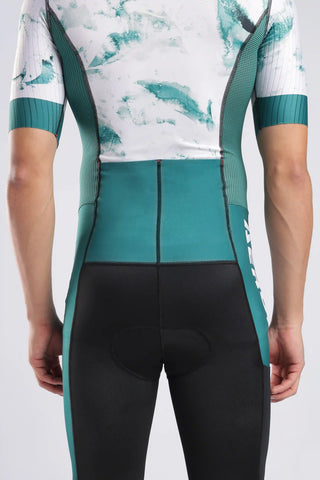 Rear view of a person wearing a fitted Aerodoc Aquaflow  trisuit onepiece for cycling running and swimming. white and green and black color combination premium fitting trisuit. The trisuit is white with teal abstract brushstroke panels and teal sleeve cuffs, while the shorts are black with teal side panels.