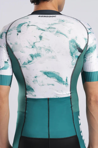 Rear view of a cyclist wearing an Aerodoc trisuit with a white and teal abstract pattern and a solid teal lower back panel.