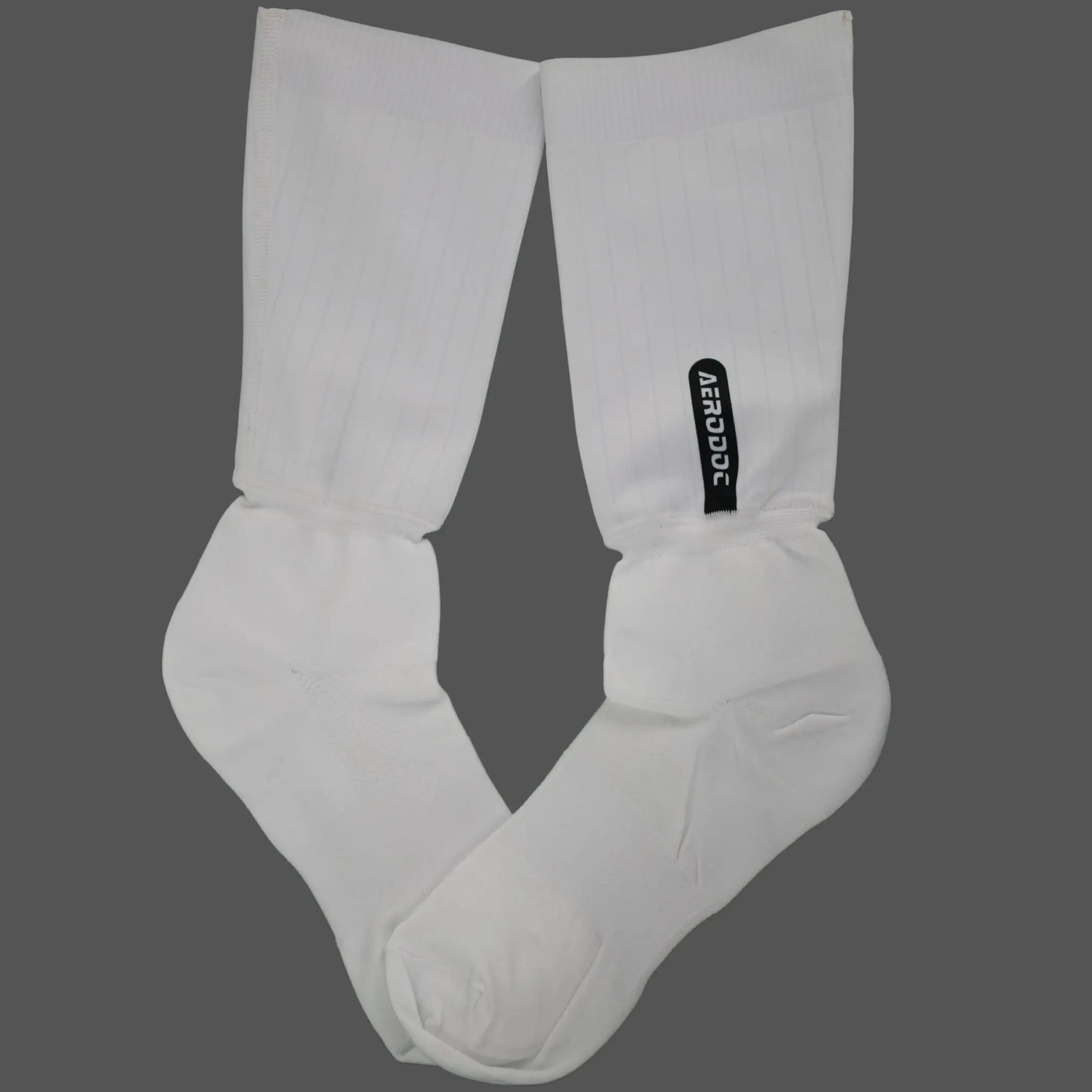 A pair of white crew socks laid flat on a solid dark gray background, featuring a small black vertical brand tag on the right sock.