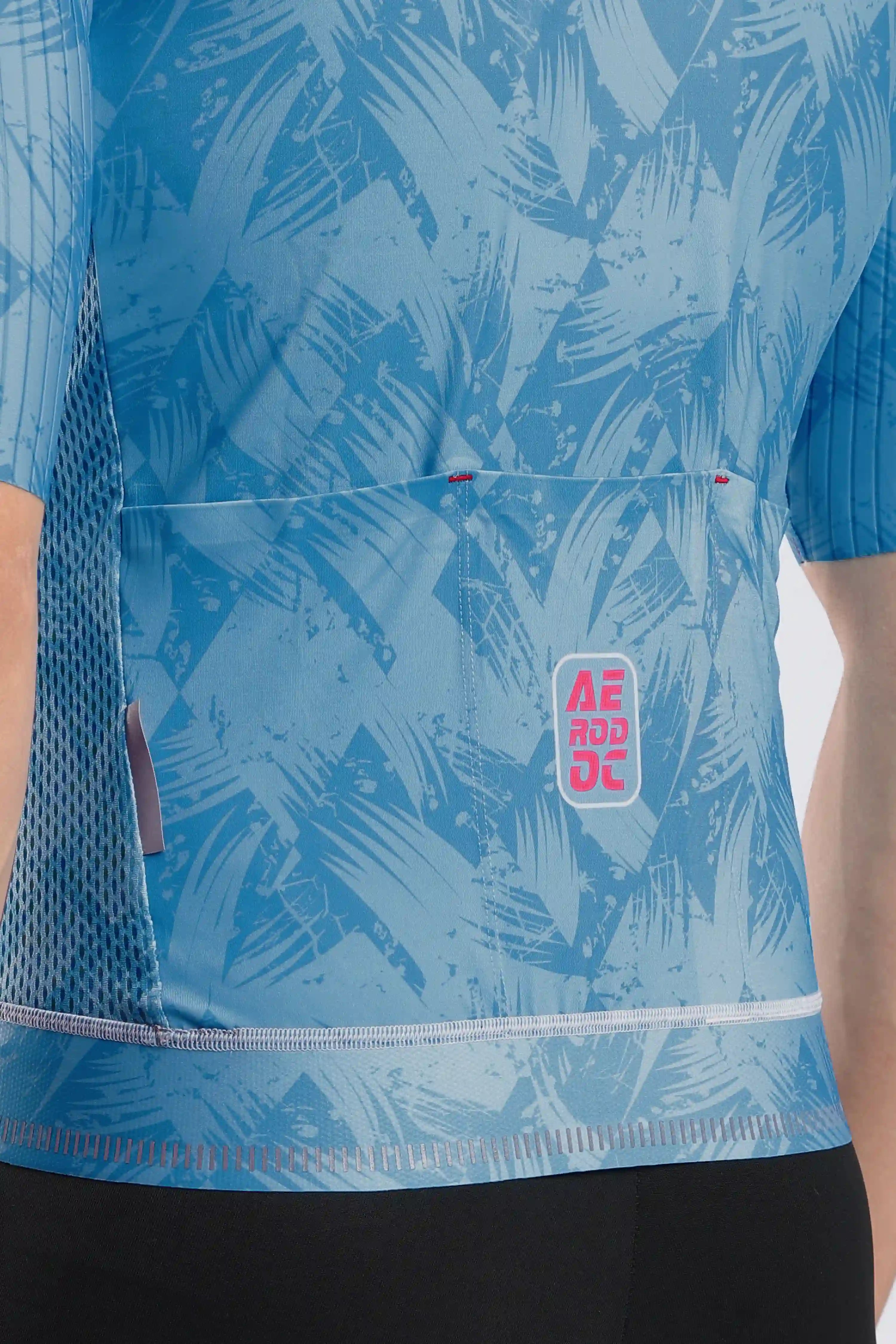 Close-up of a blue patterned cycling jersey with a front pocket and a visible AERODOC logo patch, worn by a model.