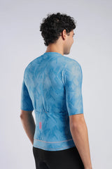 A man wearing a light blue short-sleeve cycling jersey with a subtle abstract pattern, shown from the back against a light gray studio background.