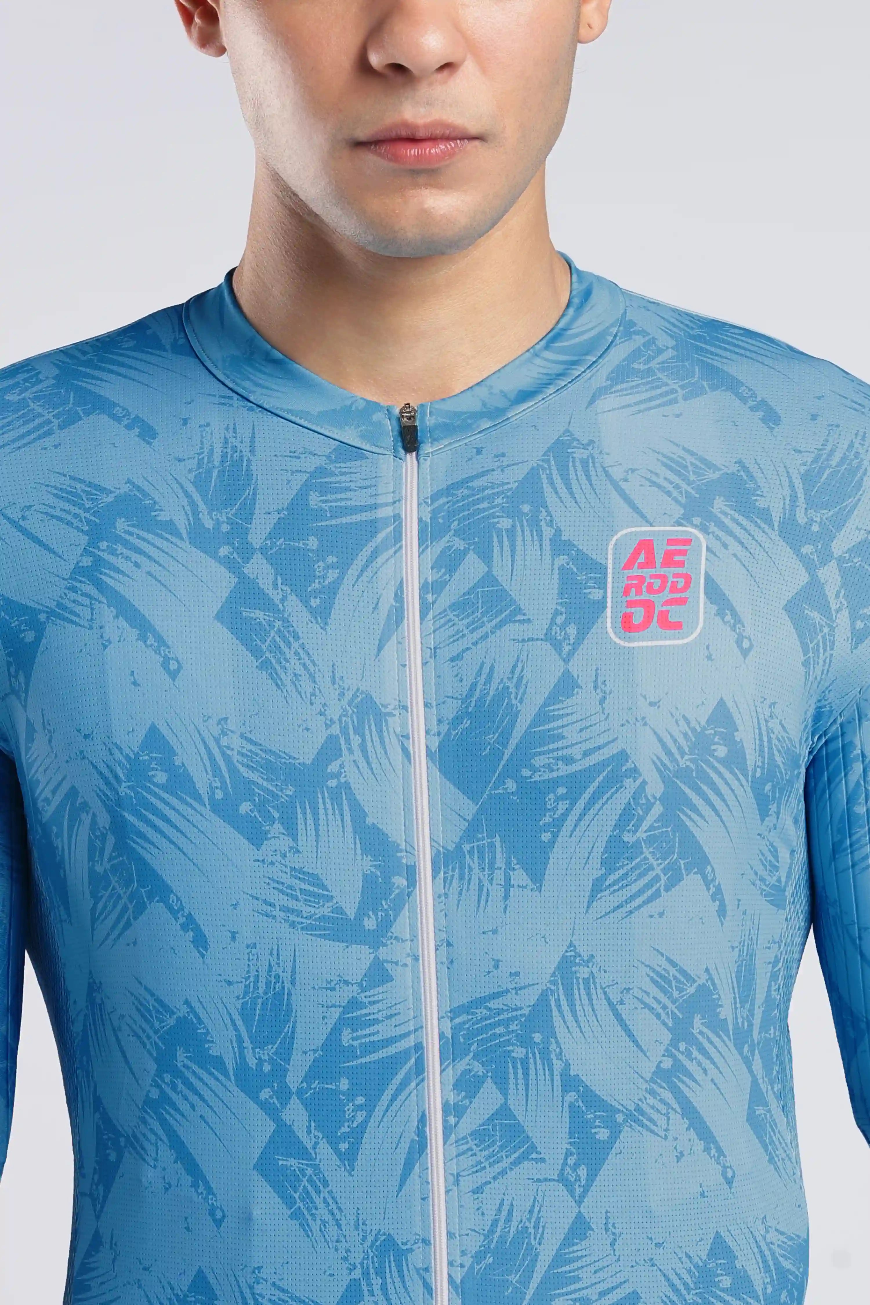A close-up of a man wearing a light blue athletic zip-up jersey with a darker blue abstract leaf pattern and a pink and red AERODOC logo on the chest.