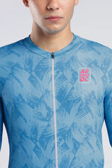 A close-up of a man wearing a light blue athletic zip-up jersey with a darker blue abstract leaf pattern and a pink and red AERODOC logo on the chest.