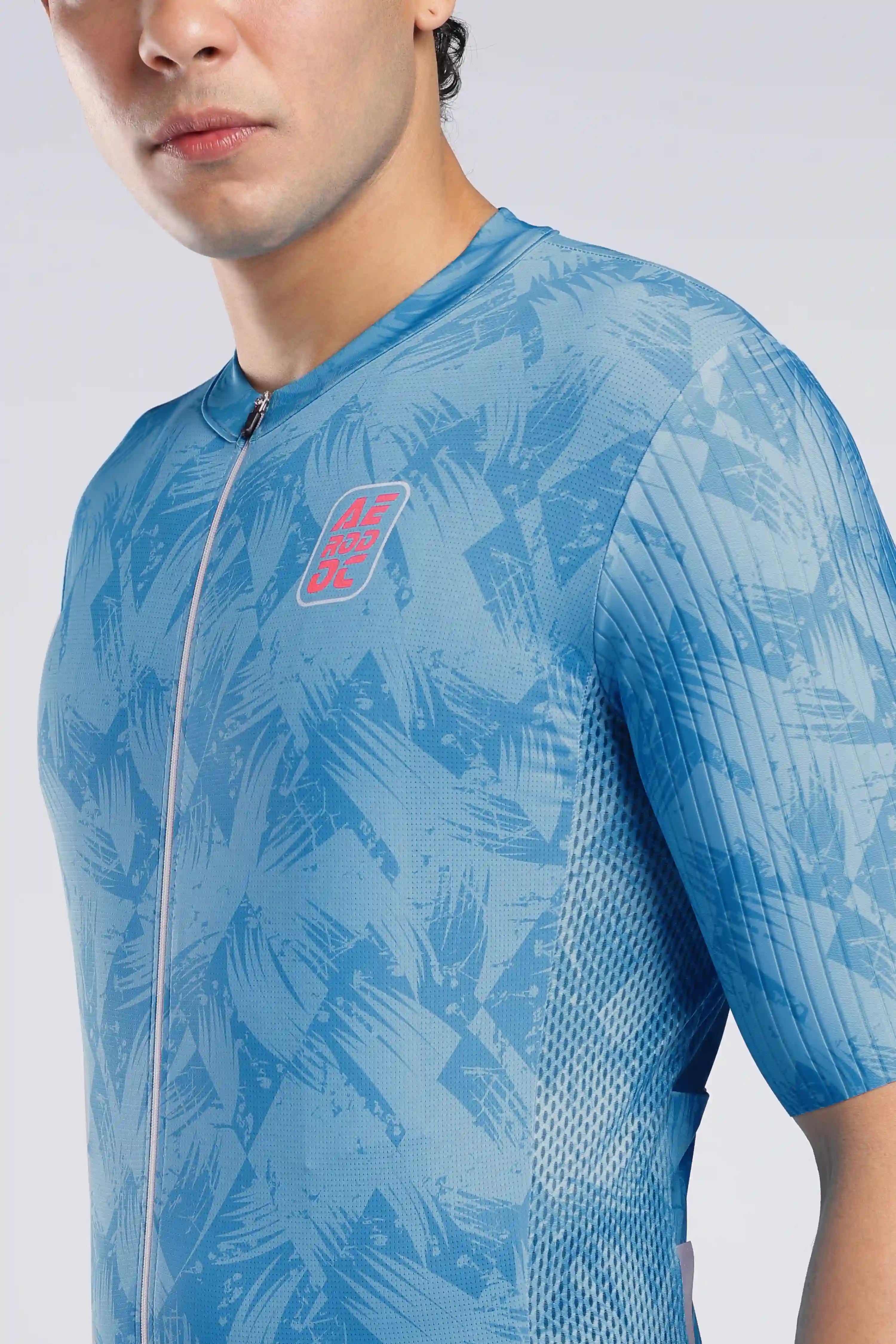 A close-up of a man wearing a light blue short-sleeve cycling jersey AERODOC red color logo on chest.