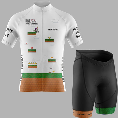 A cycling jersey and matching shorts set on a light gray background. The jersey is white with a retro video game-inspired graphic featuring green grass, brown ground, and small pixel-art elements, with black text on the sleeves and chest.