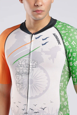 A close-up of a man wearing a short-sleeve athletic cycling or triathlon onepiece with a patriotic Indian theme. The jersey features a white center with a faint map of India and the Ashoka Chakra, an orange sleeve on the left, a green sleeve on the right with Devanagari script, and thin orange, white, and green .