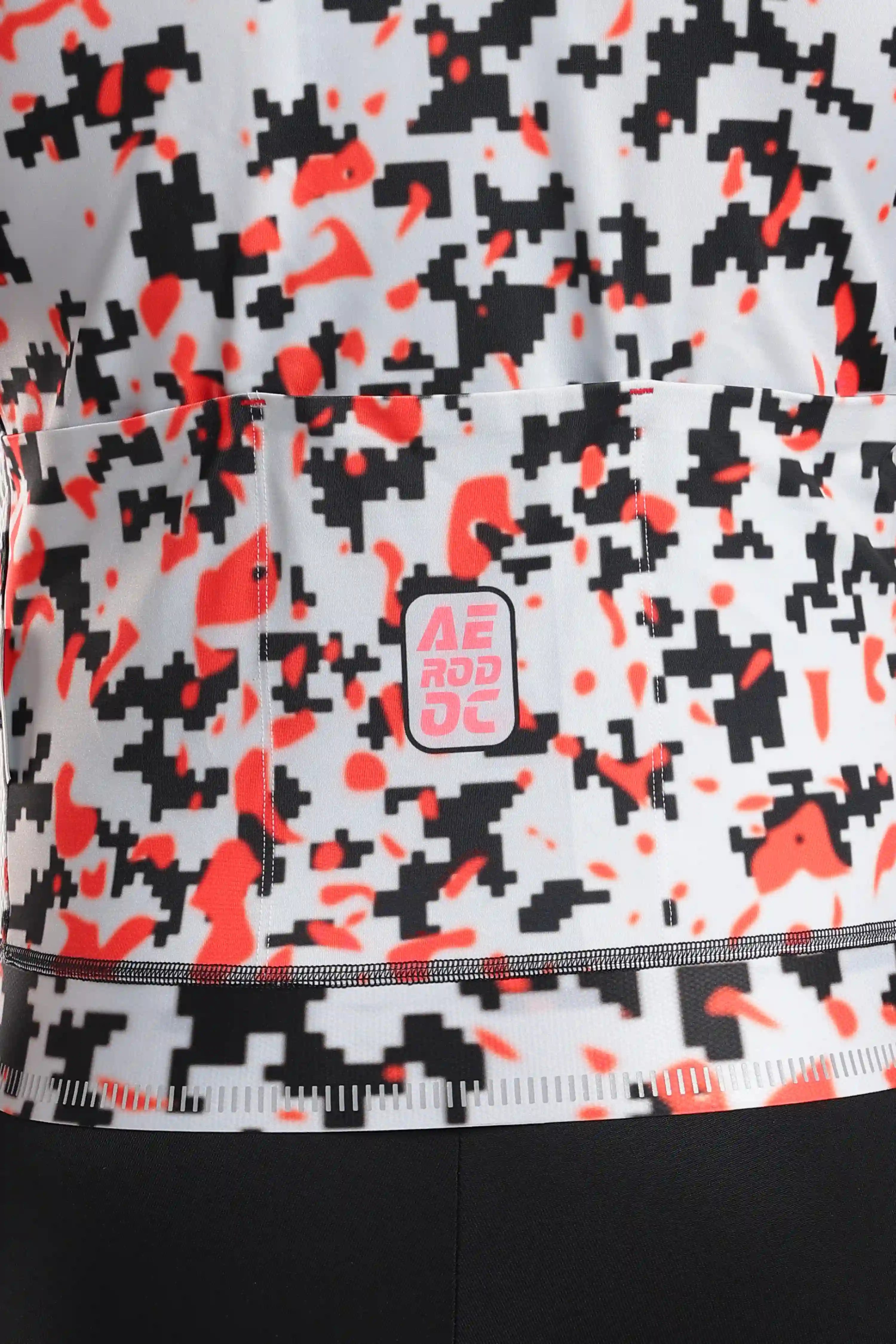 Aerodoc glitch Close-up of a cycling jersey with a black, white, and bright orange pixelated camouflage pattern.