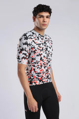 A man wearing a short-sleeve aerodoc glitch cycling jersey with a black, white, and red pixelated camouflage pattern, paired with black cycling shorts, against a light gray studio background.