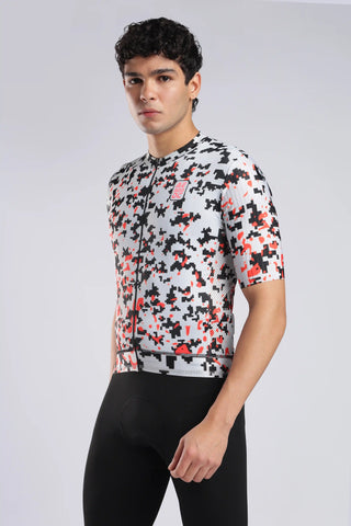 A man wearing a short-sleeve aerodoc glitch cycling jersey with a black, white, and red geometric pixelated pattern, paired with black cycling shorts, against a light gray studio background.