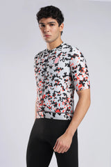 A man wearing a short-sleeve aerodoc glitch cycling jersey with a black, white, and red geometric pixelated pattern, paired with black cycling shorts, against a light gray studio background.