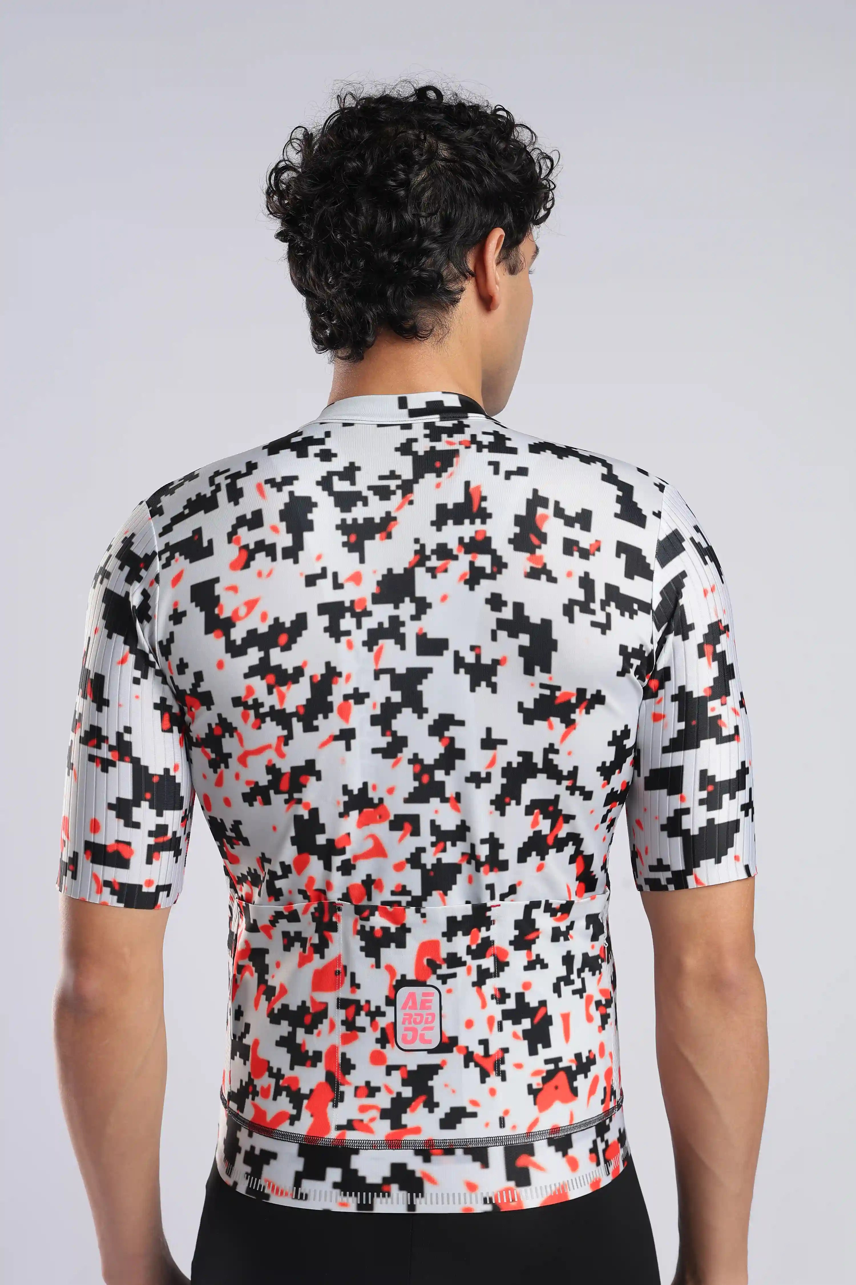 Aerodoc Rear view of a man wearing a short-sleeve cycling jersey with a black, white, and red digital camouflage pattern, set against a light gray studio background.