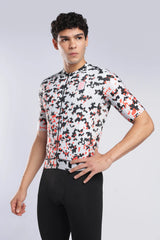 A man modeling a short-sleeve cycling jersey with a white, black, and red camouflage pattern, paired with black cycling tights, against a light gray studio background.