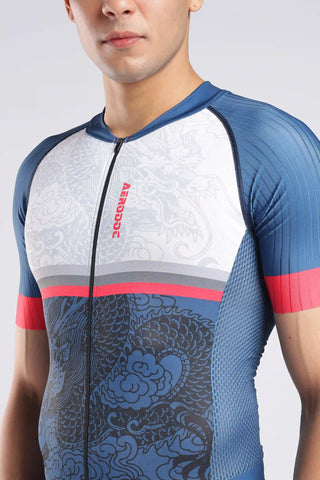 A close-up of a man wearing a short-sleeve trisuit with a white upper section, blue lower section, and dragon pattern. The aerodoc trisuit features a vertical red 'AERODOC' logo on the chest.